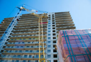 A high-rise condo building under construction in Miami with a large blue crane and construction materials in the foreground.